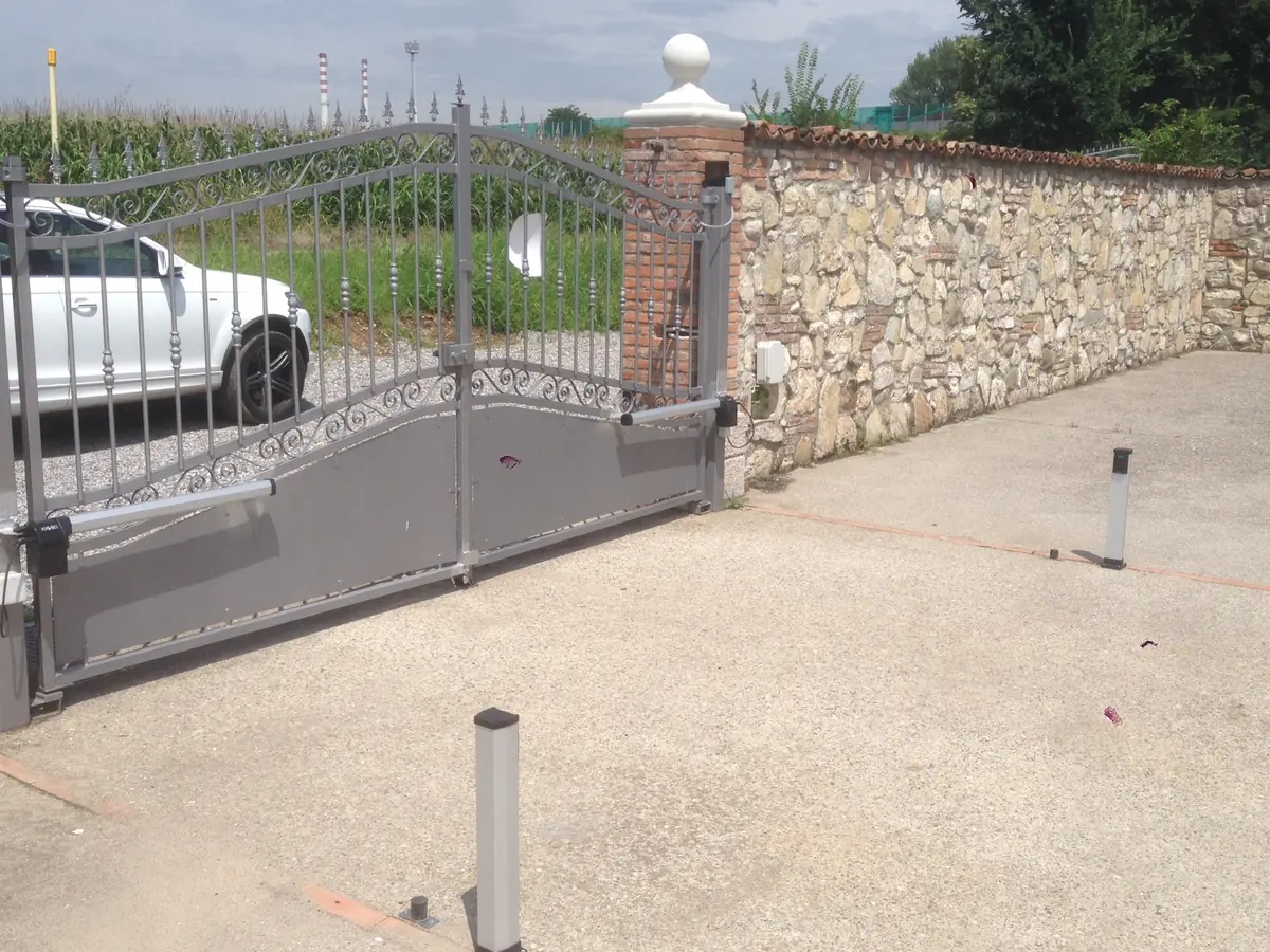 Cancello a battente motorizzato, aperto, inserito in un muro di cinta in pietra