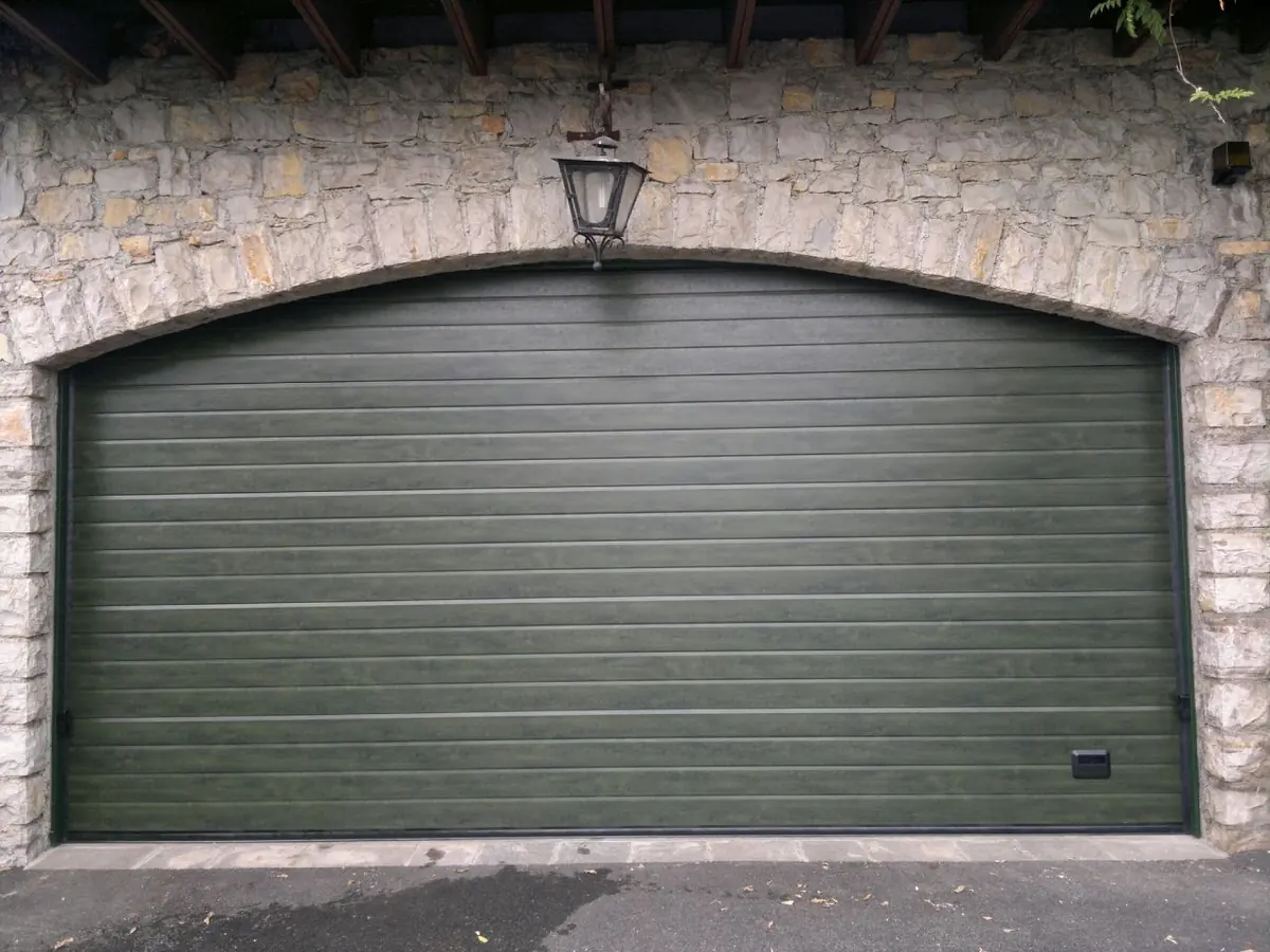 Portone sezionale verde in un vano ad arco in pietra