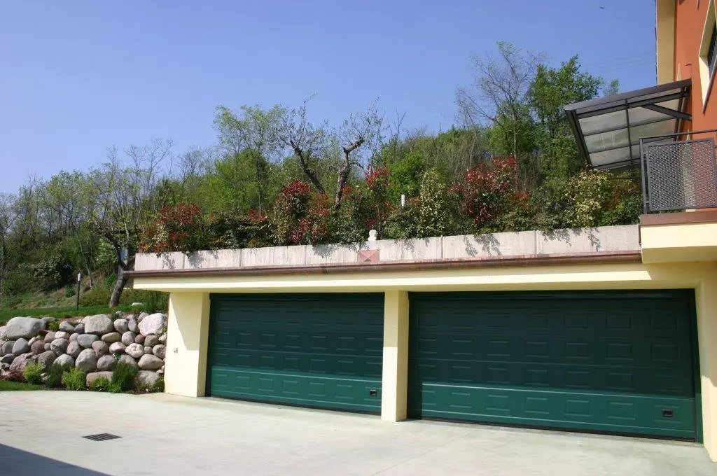 Due portoni sezionali verdi su un garage doppio in collina